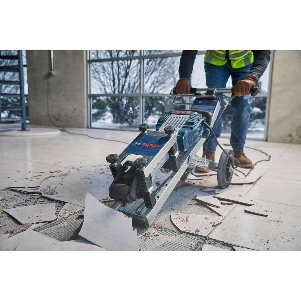 Action shot of a worker operating the Bosch floor removal cart equipped with a demolition hammer to scrape tiles off a concrete floor in a commercial space.