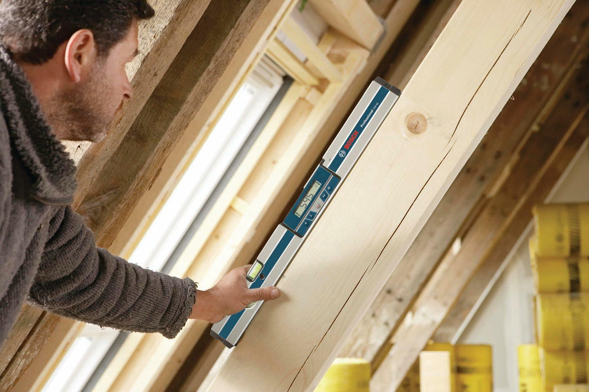 Construction worker using the Bosch GIM60 digital level to measure the 54.5 angle of a wooden roof rafter or structural beam during framing