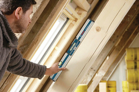 Construction worker using the Bosch GIM60 digital level to measure the 54.5 angle of a wooden roof rafter or structural beam during framing