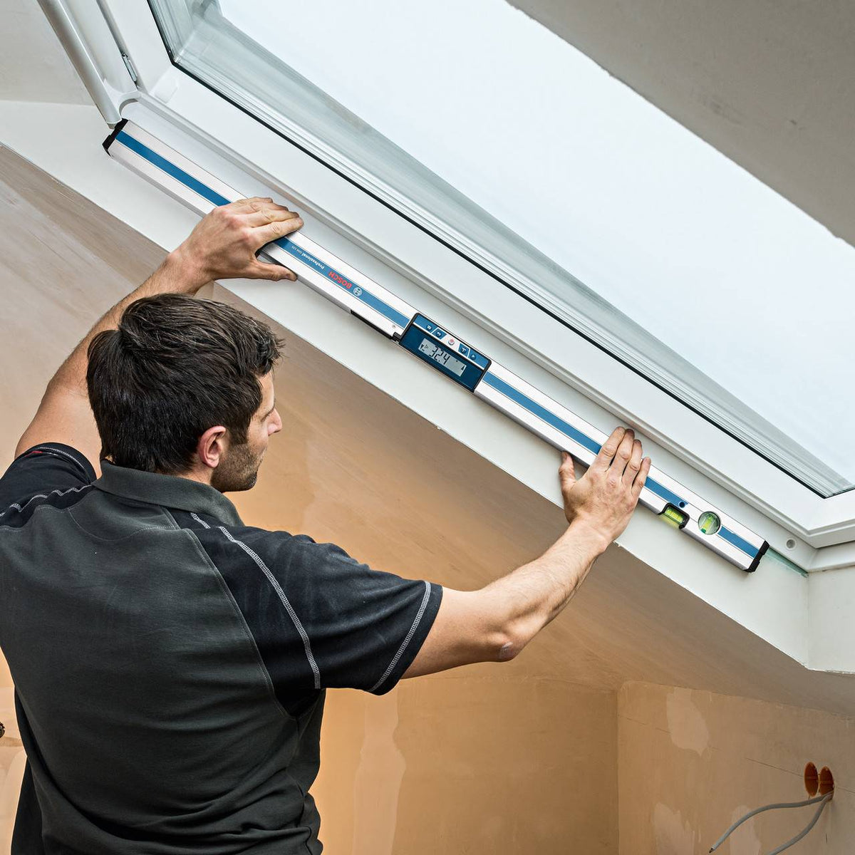 Individual checking skylight window frame alignment with spirit level; installed in sloped ceiling during renovation.
