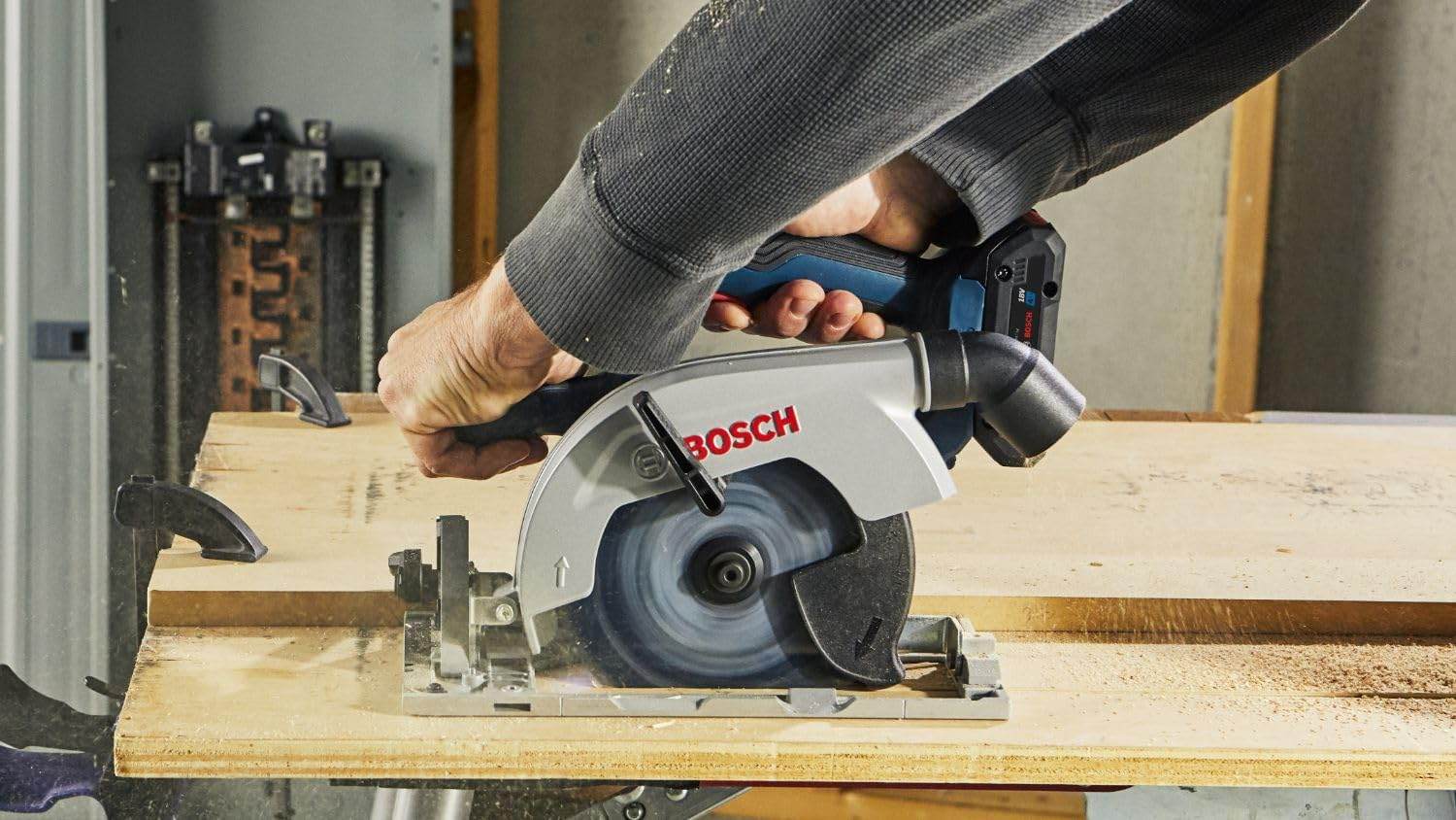 An action shot of a person using the Bosch circular saw to cut a piece of plywood on a jobsite, showing the blade-left design providing a clear view of the cut line for the right-handed operator.