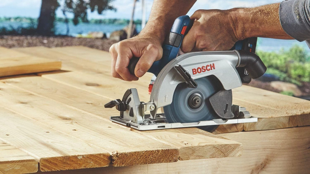 A person using the cordless circular saw to cut through thick wooden planks outdoors, with the 360-degree dust port directing debris away from the cutting surface.