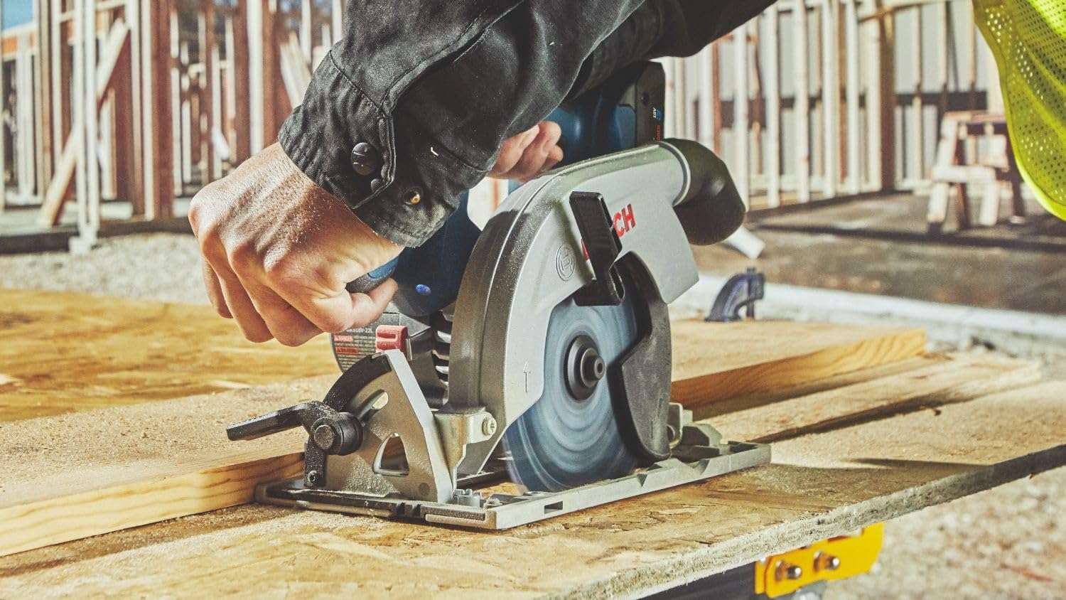 A close-up view from the front-left of the saw as it cuts through a sheet of OSB, demonstrating the stability provided by the wide metal footplate and auxiliary handle.