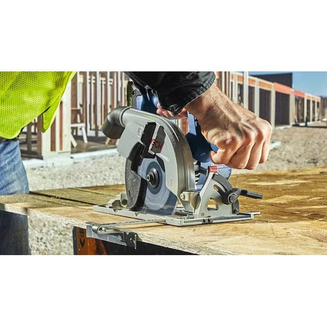 Worker in high-visibility vest using Bosch circular saw at construction site; guiding tool through wood surface.