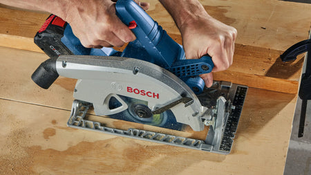 An elevated top-down action photo highlighting a tradesman utilizing two hands to guide the unibody magnesium footplate of the Bosch GKS18V-25C cordless framing saw across a wide sheet of construction plywood veneer, showing smooth tracking and a clean kerf line.