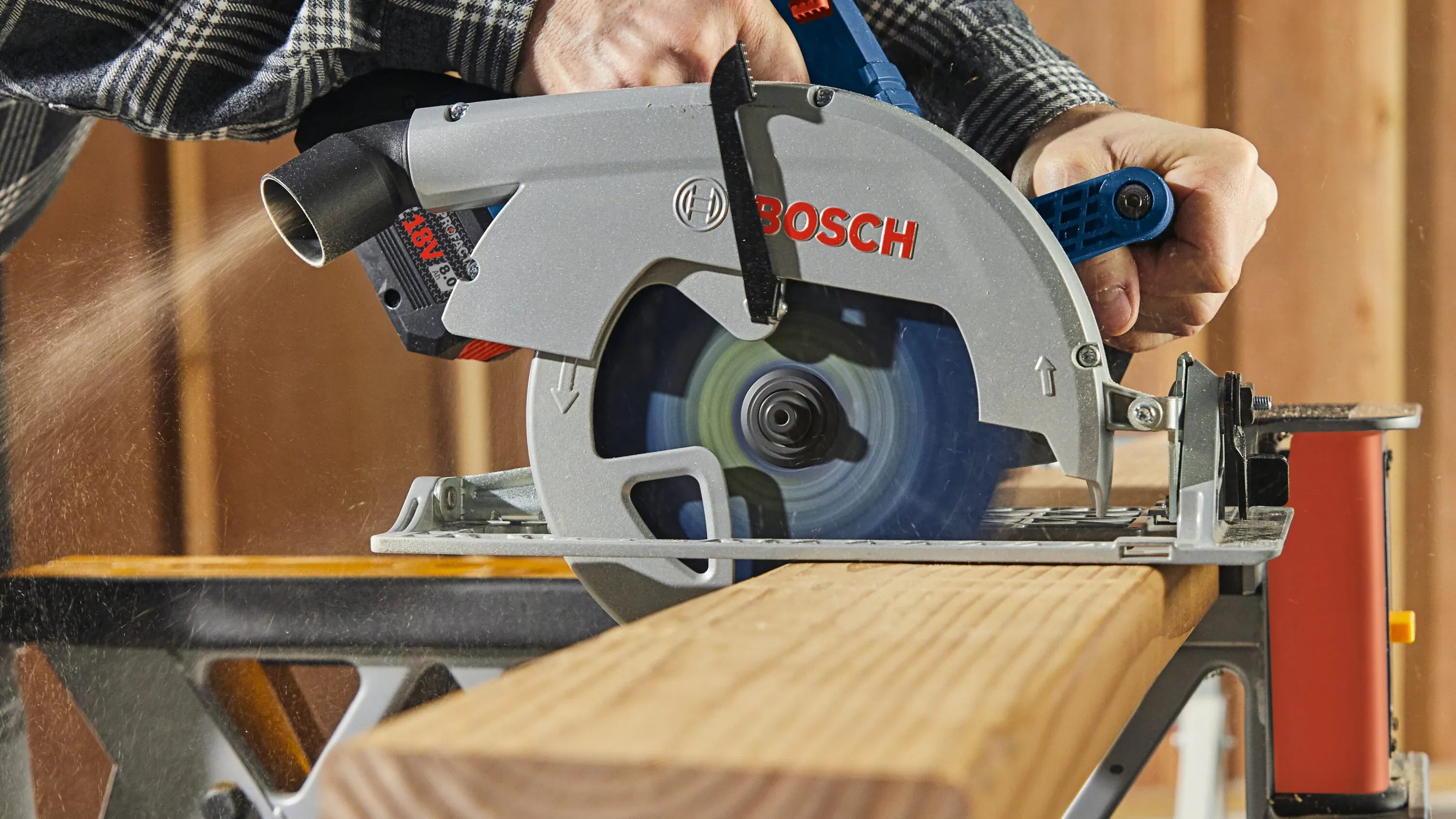 A close-up action view of a worker's hands guiding the Bosch 7-1/4 inch circular saw along a thick dimensional structural timber beam, showing a dense stream of sawdust venting out from the 360-degree pivoting extraction port while the carbide blade turns at high velocity.