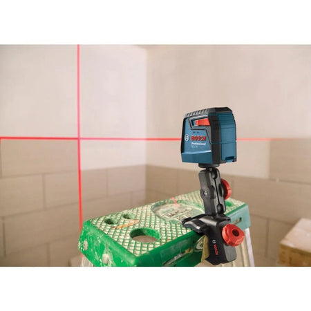 A studio shot demonstrating the Bosch GLL30 laser level clamped to a green step ladder using the MM 2 flexible mount, projecting a red cross-line against a tiled wall for precise layout.