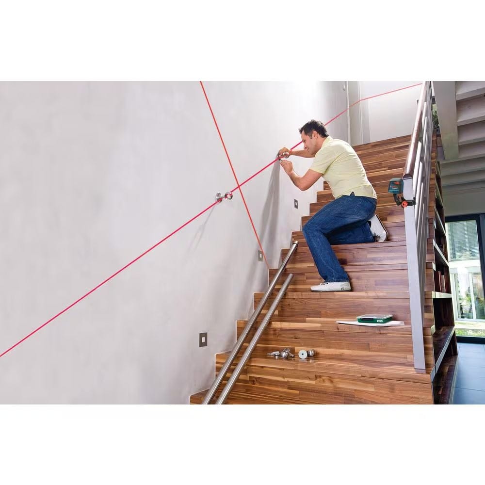 An action shot of a professional installer using the Bosch GLL30 laser clamped to a staircase railing to project a diagonal red laser line for precise handrail alignment.