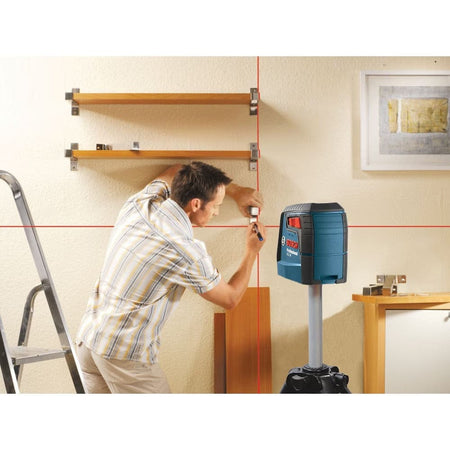 An action shot of a professional installer using the Bosch GLL30 red beam laser level to perfectly align and level floating wooden shelves on a residential wall.