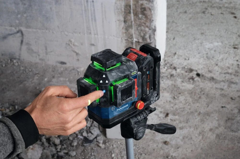 A finger pressing the Bluetooth button on the keypad of the laser level while it is mounted on a tripod in a dusty jobsite environment
