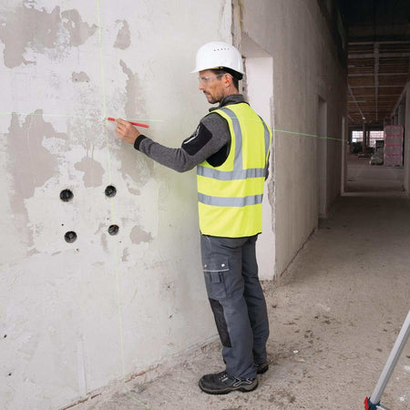 A construction worker in a safety vest marking a wall along the green laser beam projected by the tool