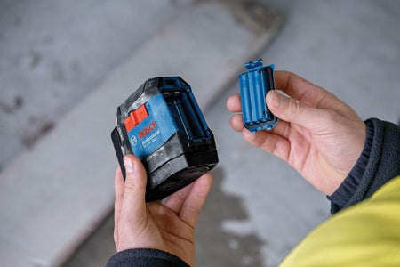 Person holding Bosch battery pack and blue cartridge component in a workshop setting, demonstrating power setup for Bosch tools.