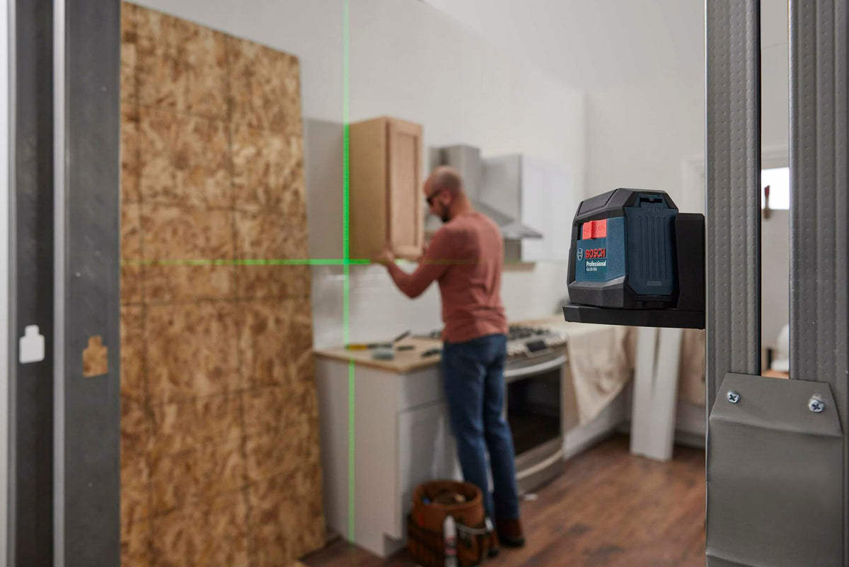 Installer using Bosch green beam laser level in a kitchen, with horizontal and vertical lines projected for precise cabinetry alignment.