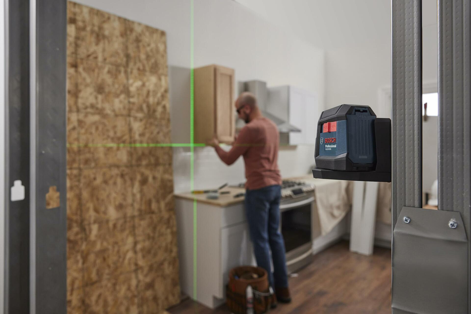 Installer using Bosch green beam laser level in a kitchen, with horizontal and vertical lines projected for precise cabinetry alignment.