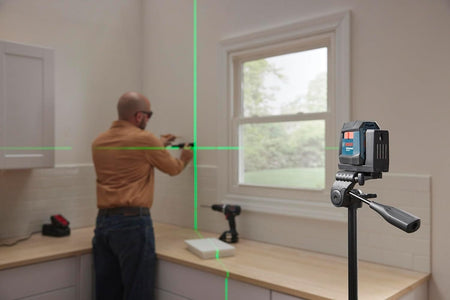 Interior view of the laser level mounted on a tripod, projecting bright green cross-lines onto a white wall to guide cabinet installation.