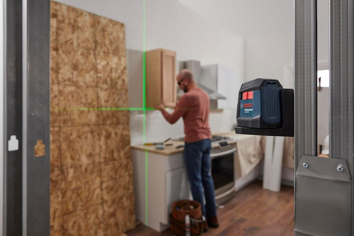 Application shot of the laser level magnetically attached to a metal door frame, projecting level horizontal and vertical green lines across a kitchen installation area.