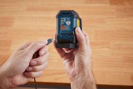 Close-up of a user plugging a USB-C charging cable directly into the charging port located on the back of the laser level unit.