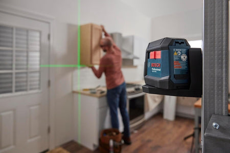 Bosch GLL3-330CG laser level projecting green cross-lines across kitchen; man uses beams to align cabinet installation.