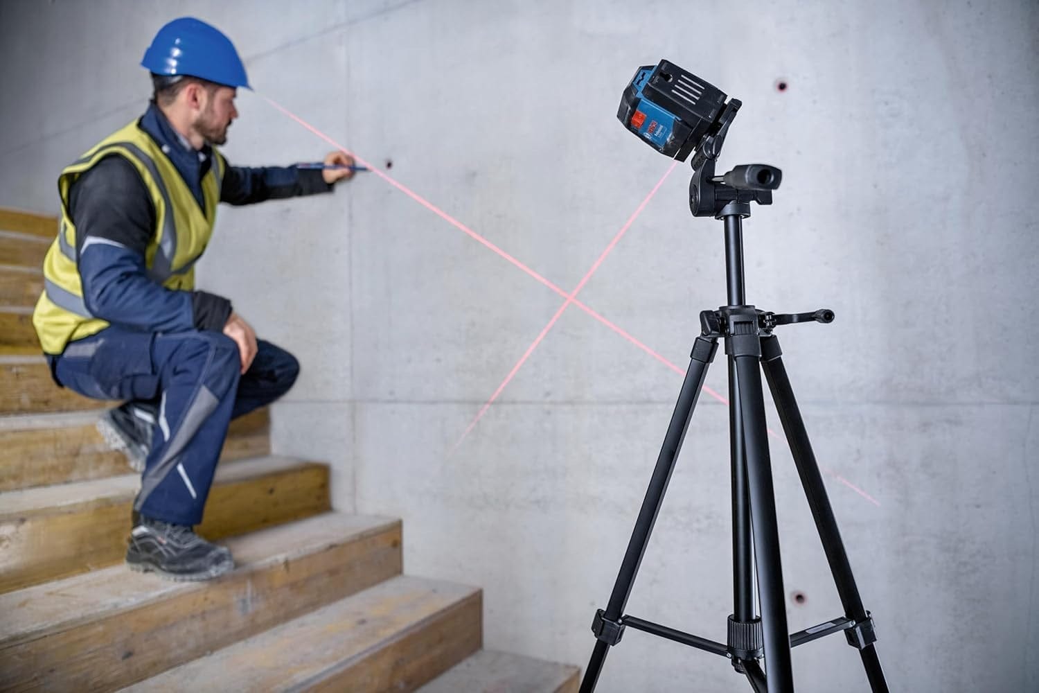 The Bosch GLL50-20 cross-line laser mounted on a professional tripod in manual tilt mode, projecting angled red beams for marking layout points on a concrete staircase.