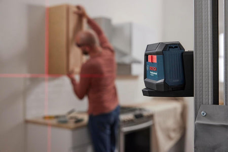 A professional using the Bosch GLL50-20 laser level mounted to a metal stud to align and install wooden cabinets in a residential kitchen.