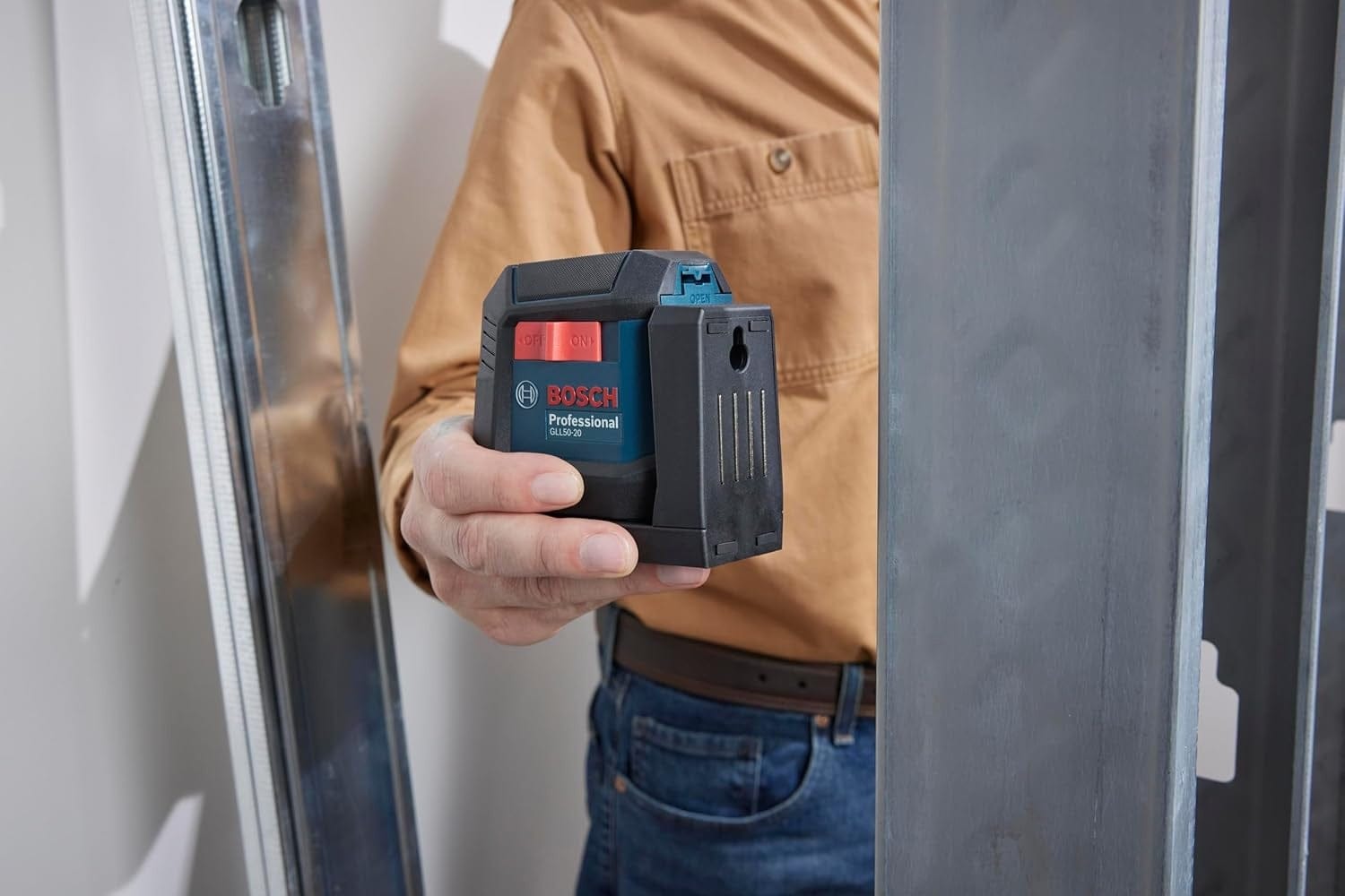 A person's hand holding the Bosch GLL50-20 laser level against a metal wall stud, demonstrating the strength and utility of the tool's integrated multipurpose magnetic mount.