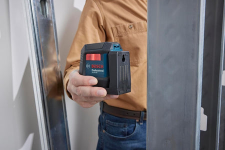 A person's hand holding the Bosch GLL50-20 laser level against a metal wall stud, demonstrating the strength and utility of the tool's integrated multipurpose magnetic mount.