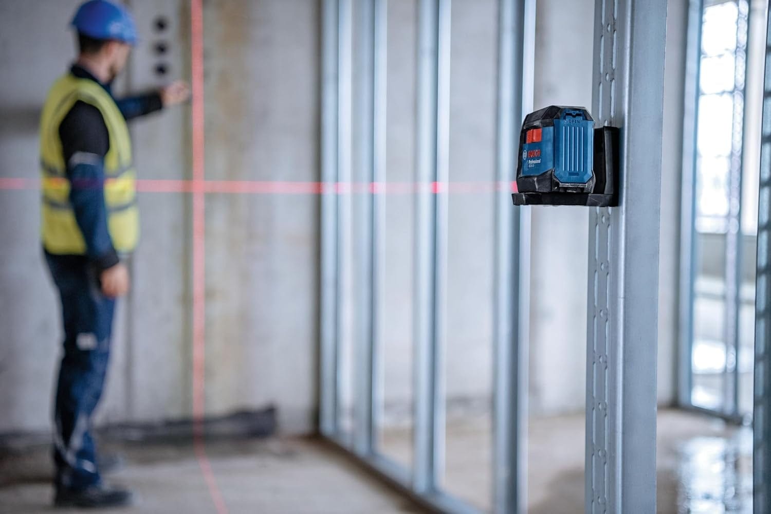 A worker on a commercial jobsite using the Bosch GLL50-20 laser level magnetically attached to a vertical steel track to project leveling lines across a large room.