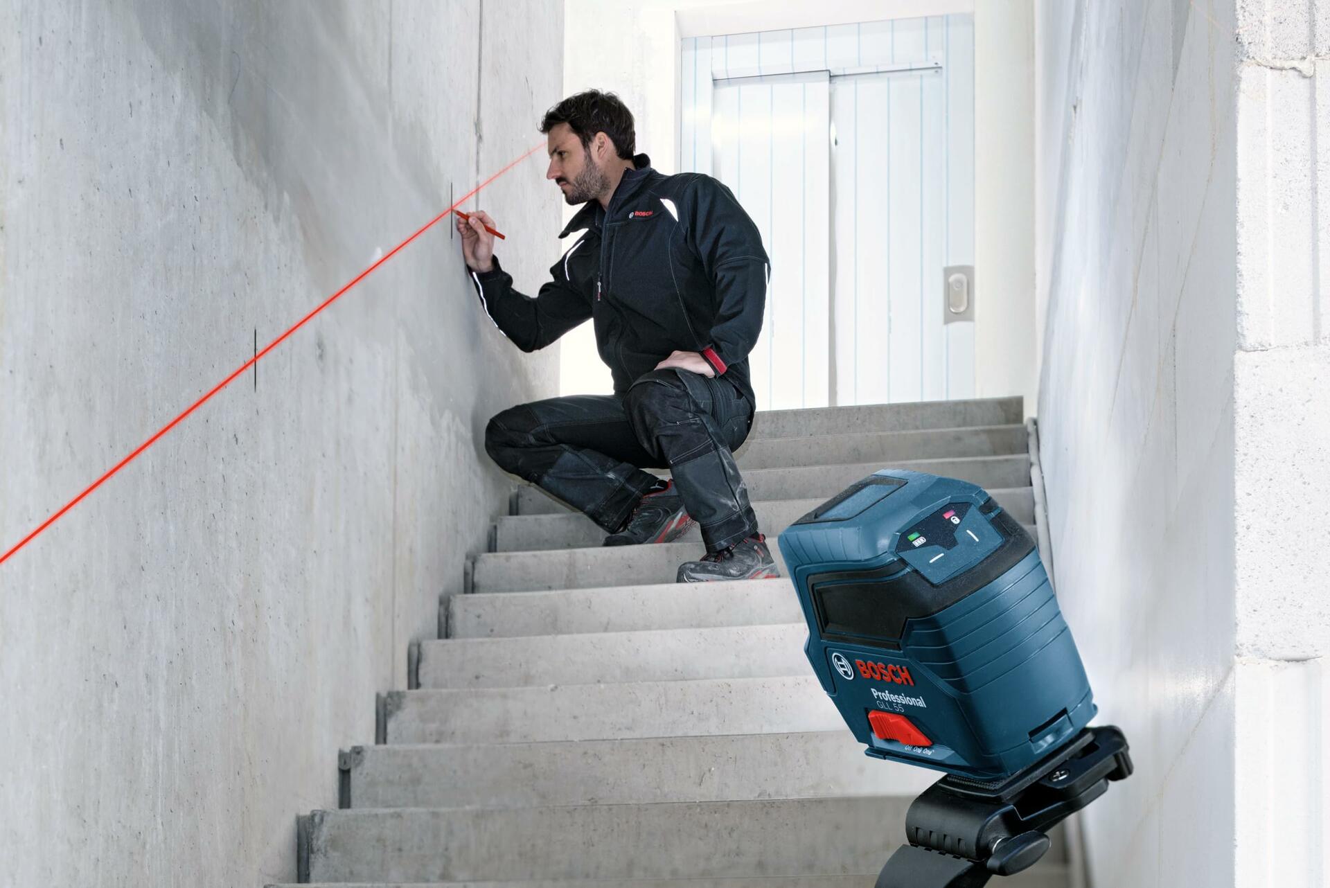 A construction professional using the Bosch GLL 55 laser level mounted on a tripod to mark precise points along a concrete staircase using the red cross-line beams.