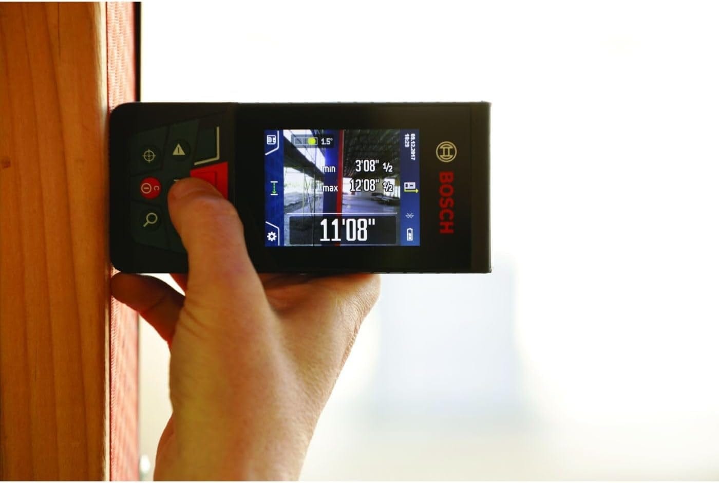 Person using Bosch GLM400CL laser measure to record distance from wooden surface; screen displays 11'08" and angle data.