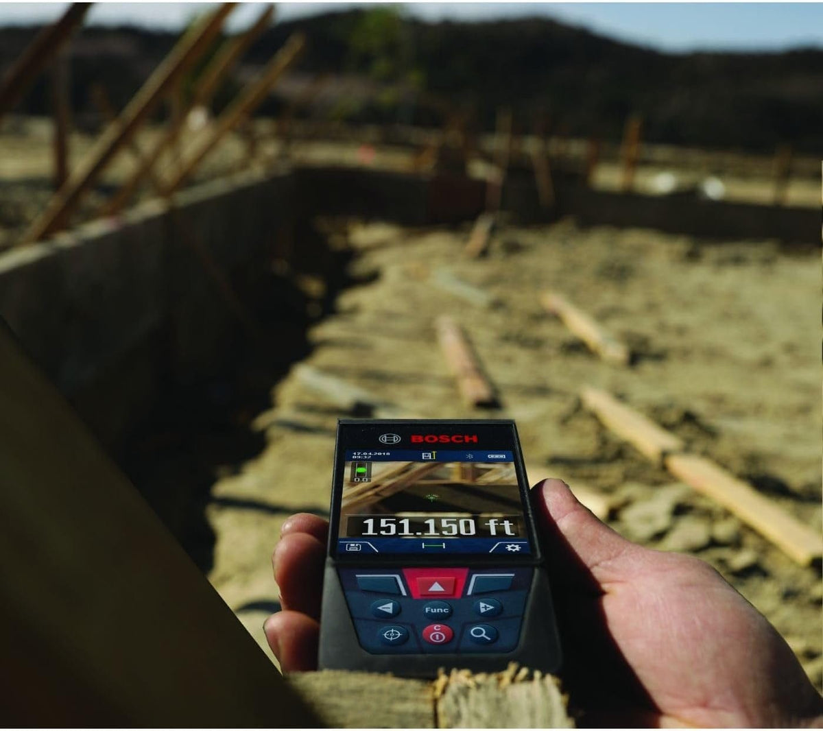Bosch GLM400CL laser measure held at construction site; screen shows 151.150 ft reading with visual targeting display.