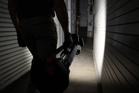A worker carrying the collapsed Bosch tower light by its integrated handle through a dimly lit hallway, demonstrating the tool's portability.