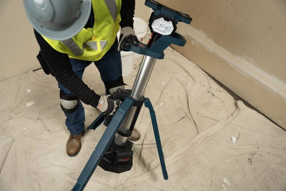 A close-up view of a worker's hands deploying the tripod legs of the tower light onto a drop cloth-covered floor.