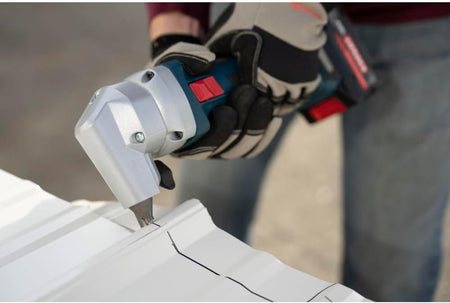 An action shot of a sheet metal worker wearing heavy-duty padded work gloves using the Bosch 18V cordless nibbler to punch a precise straight path across a ribbed white corrugated roofing panel along a pre-marked black marker guidance line.