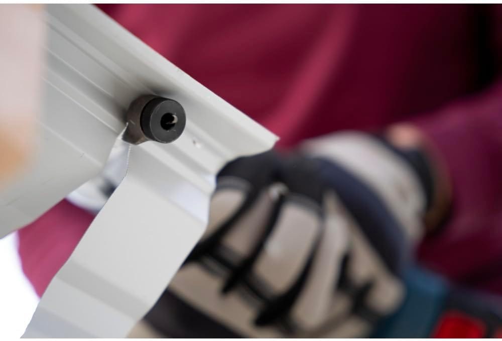 A close-up under-panel view highlighting the underside of the Bosch nibbler's punch mechanism as it cuts smoothly through a white-coated corrugated structural steel sheet, detailing the tool-free rotating die orientation with a worker in the background.