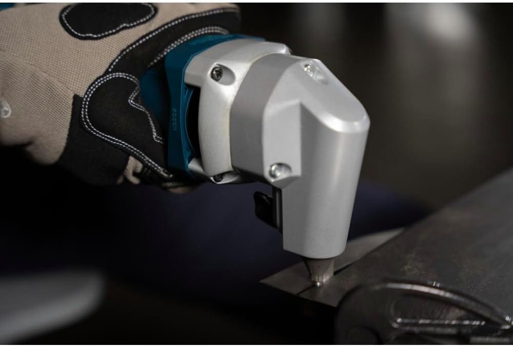 A close-up macro action shot focused on the rugged silver cast metal cutting head of the Bosch 18V nibbler as it punches a clean, burr-free linear seam directly into a heavy industrial sheet metal plate.