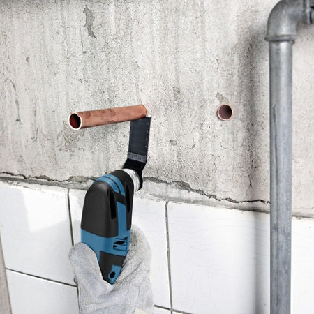 A close-up application shot of a tradesperson utilizing the Bosch cordless multi-tool with a Starlock plunge cutting saw blade to execute a precise, flush cut on a copper pipe protruding from an unfinished concrete wall above a tile line.