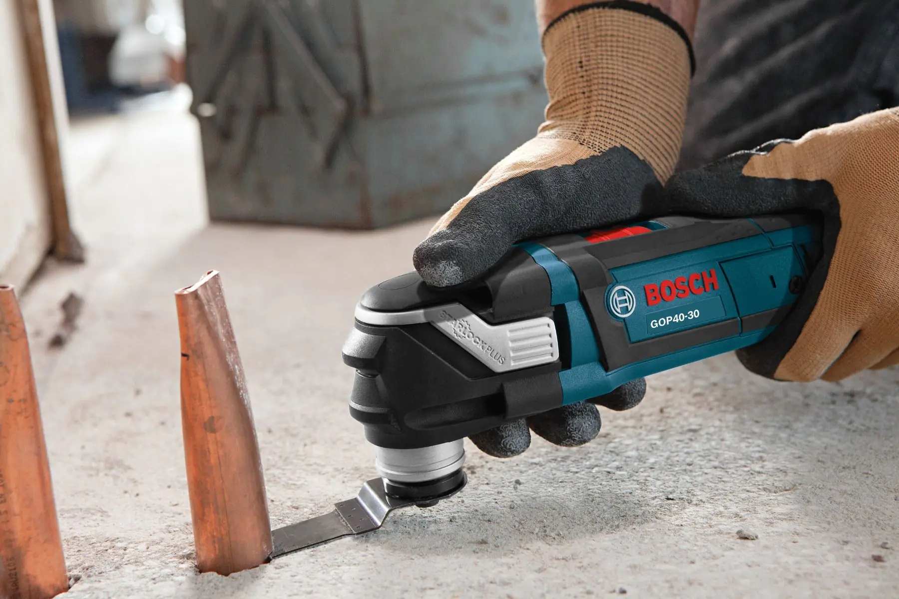 Person using Bosch GOP40-30 multi-tool to cut copper pipe protruding from concrete surface in construction setting.