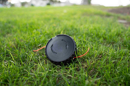 Close-up studio shot of the Bosch Pro-Tap bump-feed spool sitting in grass, illustrating the dual-line EasyWind system designed for rapid line reloading without head disassembly.