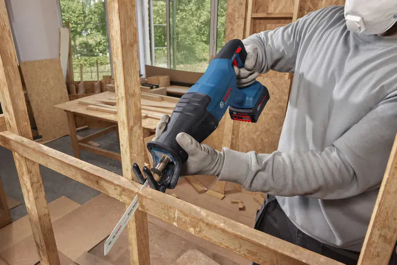 A professional contractor operating the heavy duty Bosch 18V cordless reciprocating saw bare tool to make precise cuts through a horizontal structural wood support beam. Sawdust sprays from the bi-metal demolition blade path as the tool's pivoting shoe maintains flat, stable contact against the wood framework.