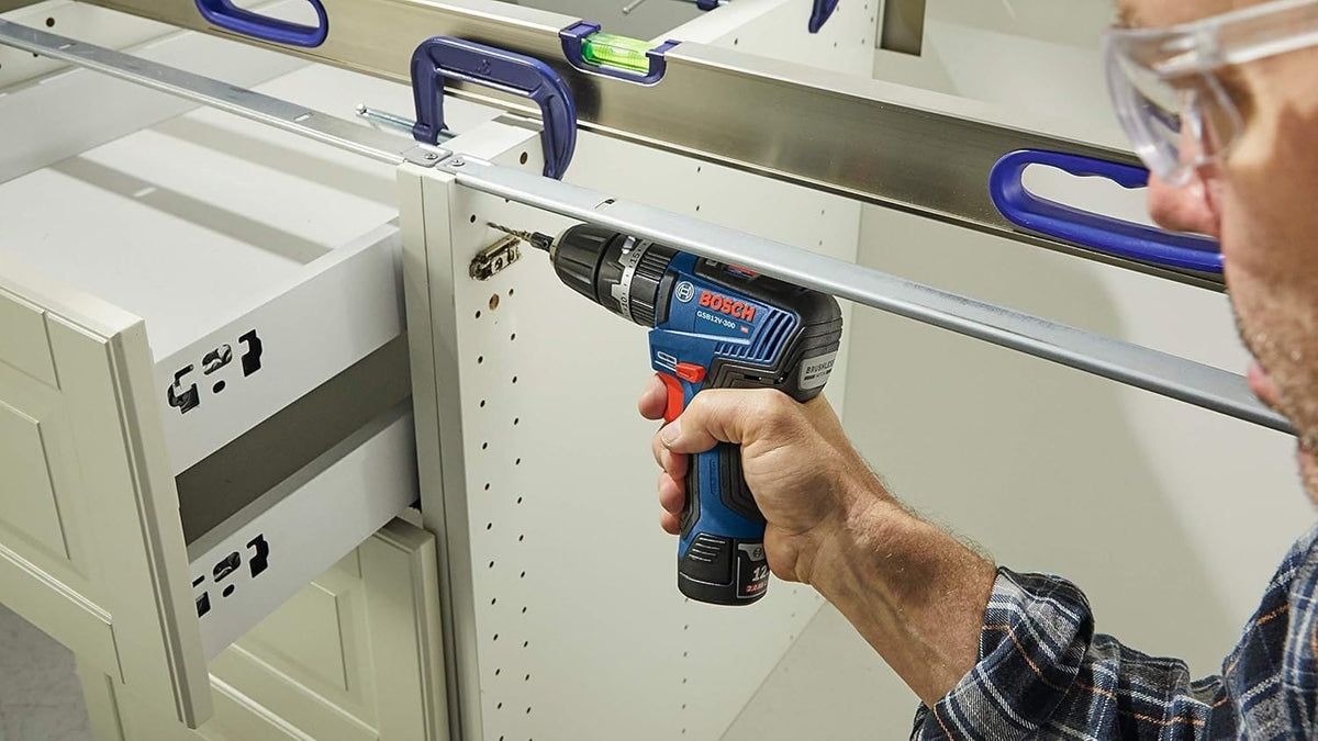 A worker using the 12V Max brushless hammer drill/driver to bore a pilot hole into a white wooden cabinet frame held together by clamps.
