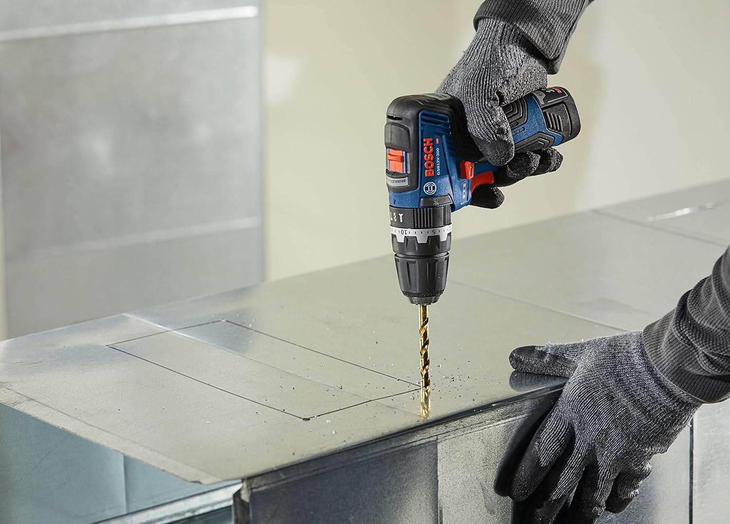 Action shot of a user wearing protective gloves using the 12V Max hammer drill/driver to bore a hole into a sheet of metal ductwork on a jobsite.