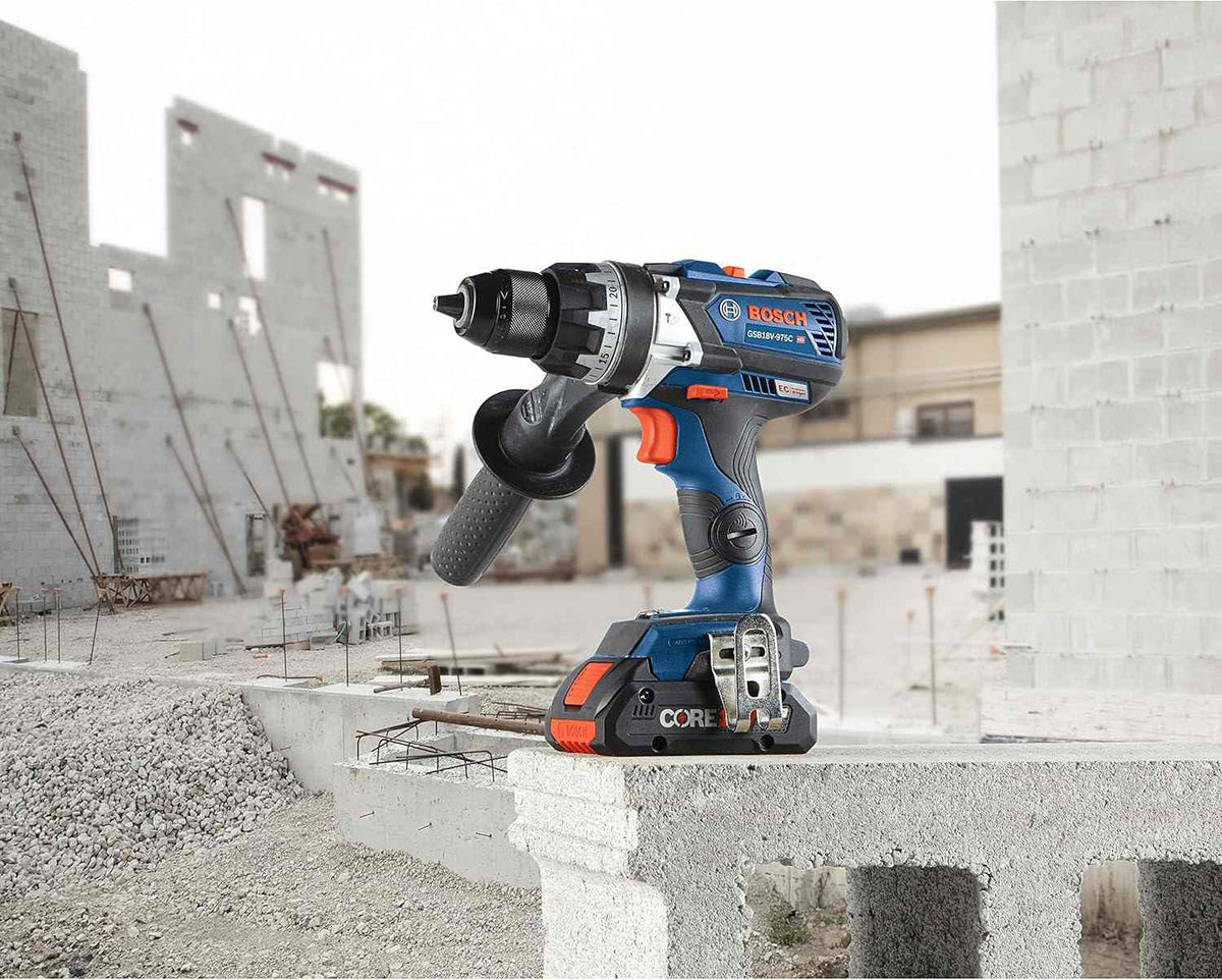 The Bosch 18V hammer drill/driver with a side handle and CORE18V battery sitting on a concrete block at a construction site.