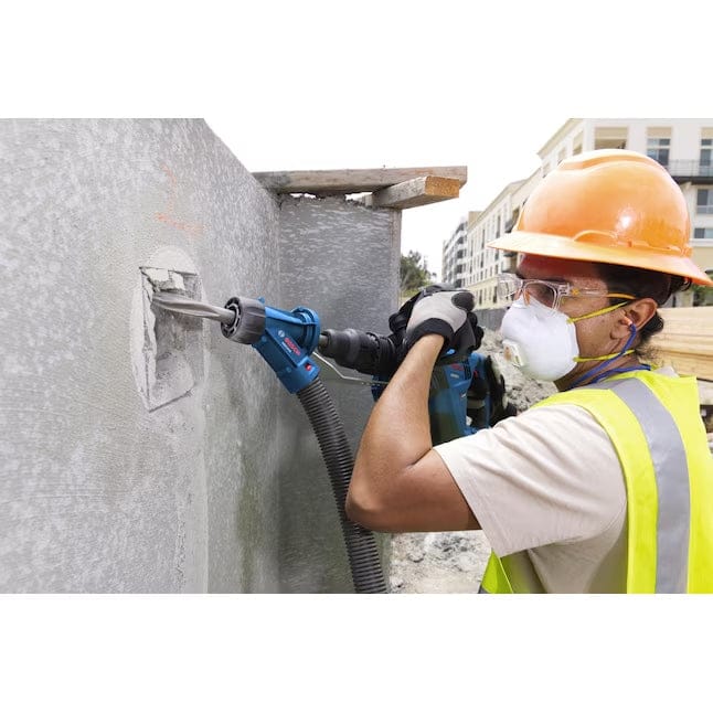 A profile view of a worker utilizing the Bosch PROFACTOR demolition hammer with a vacuum-connected dust solution to maintain a clean environment while breaking concrete.