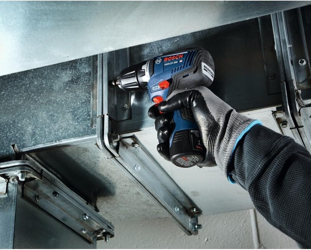 An action shot of a professional in protective gloves using the compact Bosch drill/driver to fasten a screw into a metal HVAC duct in a tight, industrial setting.