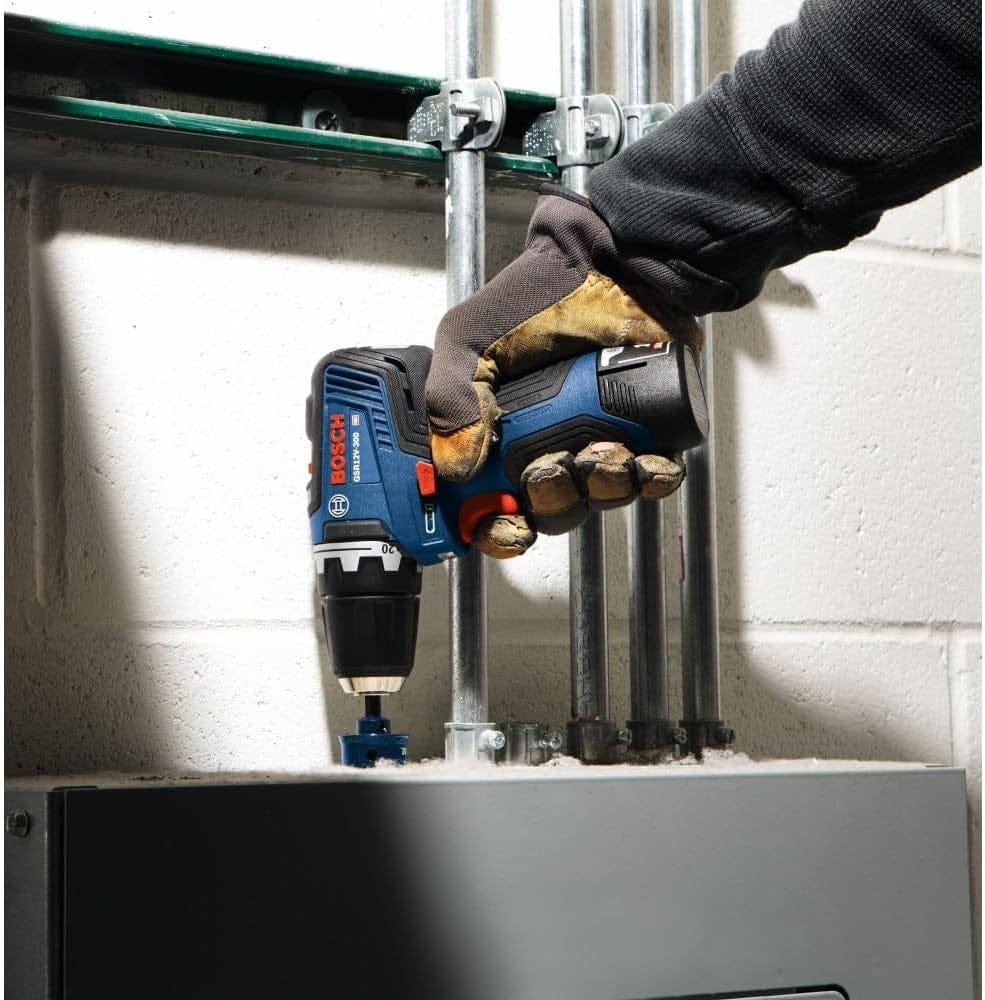A worker using the 12V Max brushless drill to bore a hole into a metal electrical junction box mounted against a white cinder block wall.