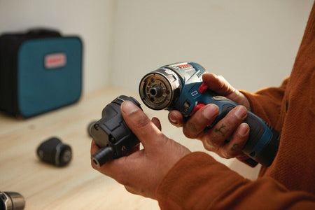 A person holding the Bosch 12V Max Chameleon FlexiClick 5-in-1 drill driver in their right hand while attaching the offset angle adapter with their left hand.