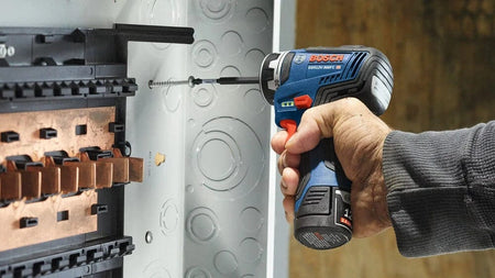 A close-up of a person holding the Bosch 12V Max Chameleon FlexiClick 5-in-1 drill driver to drive a long screw into an electrical panel box.