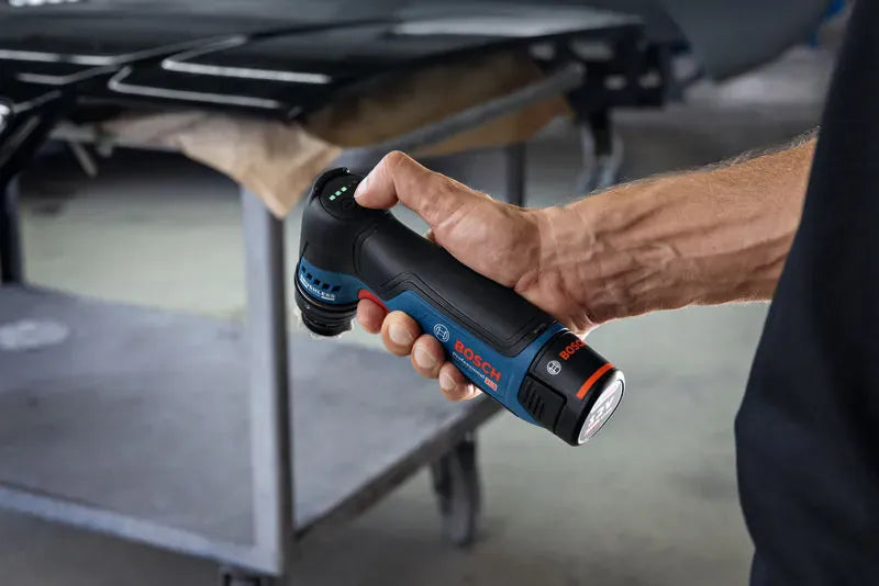 A close-up view capturing a detailer holding the Bosch GSS12V-32N 12V max detail orbital sander from the side. This graphic-free variant focuses purely on the hand holding the tool, highlighting the compact barrel grip ergonomics and active green LED indicator light bars illuminated on the top smart user interface panel.
