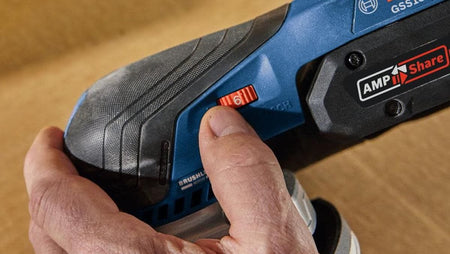 An active close-up view of a woodworker's hand adjusting the red variable speed dial wheel to setting 6 on the side of the Bosch finishing sander next to a prominent black AMPShare battery system compatibility logo label.