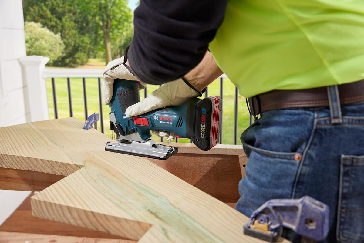 Action shot showing a worker using the 18V jig saw to cut a decorative notch into a large wooden stair stringer outdoors. The cordless design allows for maneuverability on large workpieces.